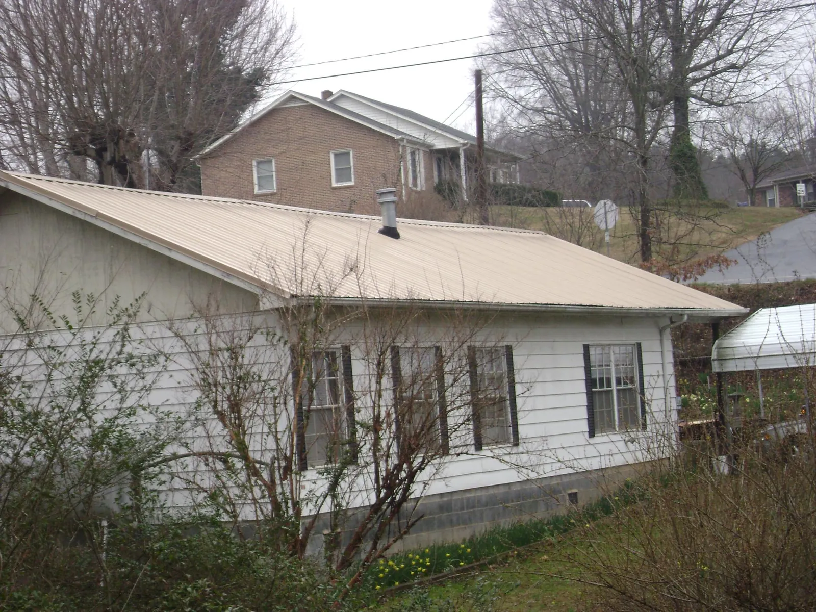 Tan metal roof on a white sided house set into a hillside — Commercial Roofing by Roofing Brothers in Brighton